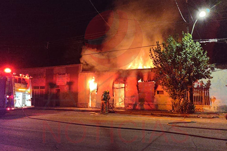 Fotografía de incendio nocturno en inmueble abandonado en Nuevo Casas Grandes, con bomberos en acción.