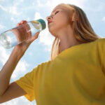 Persona bebiendo agua bajo el sol para evitar el golpe de calor en verano.