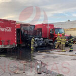 Bomberos trabajando para apagar el incendio en un camión repartidor de Coca Cola en el patio de la empresa.