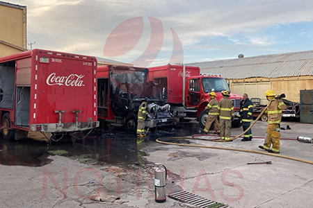 Bomberos trabajando para apagar el incendio en un camión repartidor de Coca Cola en el patio de la empresa.