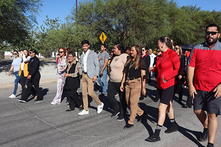 Participantes de la caminata de activación física en Nuevo Casas Grandes recorren la avenida Constitución hacia la Macro Plaza. Autoridades locales, seis instituciones educativas y padres de familia se unieron en esta actividad para promover el bienestar y la salud en la comunidad.